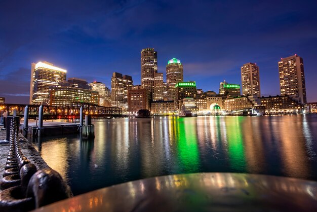 Stadt Boston mit Gebäuden und Hafen bei Nacht, Wasserreflexionen und blauem Himmel mit Sternen