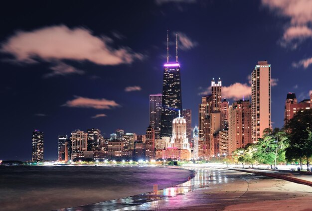 Städtischer Wolkenkratzer der Stadt Chicago bei Nacht am Seeufer in der Innenstadt, beleuchtet mit Lake Michigan und Wasserreflexion vom North Avenue Beach aus gesehen.