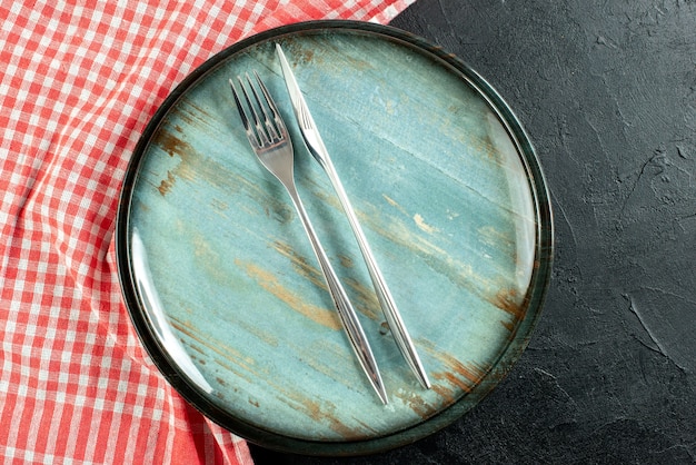 Stahlgabel und Abendessenmesser von oben auf runder Platte rot und weiß karierte Tischdecke auf schwarzem Tisch