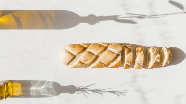 Stangenbrot mit Schatten von Olivenflaschen auf Hintergrund