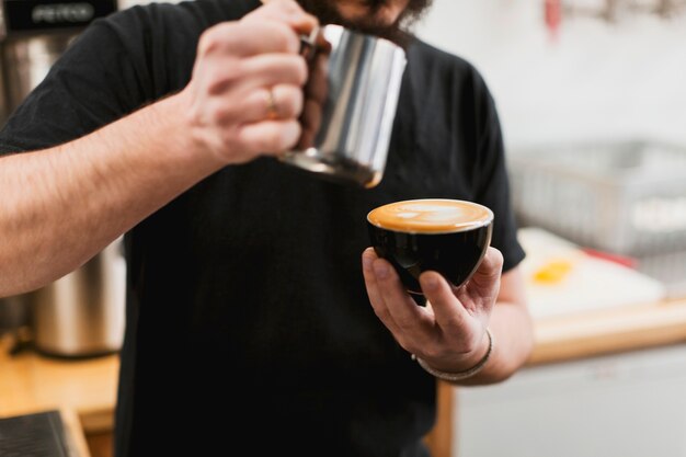 Stangenkonzept mit dem Kellner, der Milch in Kaffee einsetzt