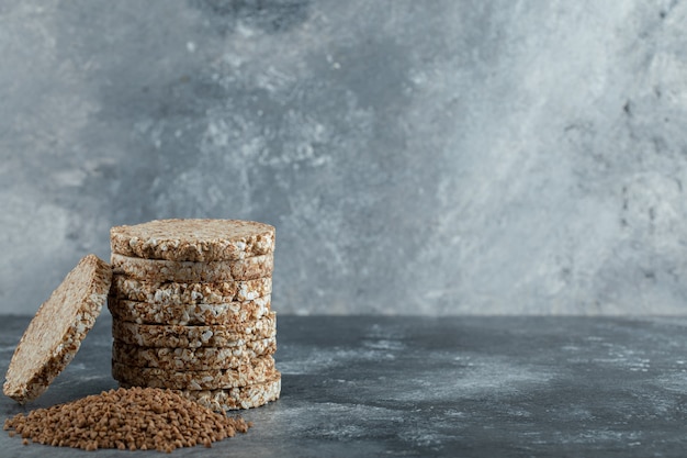 Stapel Reiskuchen und Haufen Buchweizen auf Marmoroberfläche