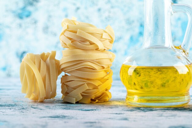 Stapel Tagliatelle-Nester und Glas Olivenöl auf Blau.