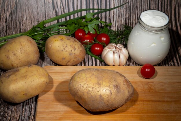 Stapel von kartoffeln, die auf einem hölzernen schneidebrett neben gemüse- und kräuterkochkonzept liegen