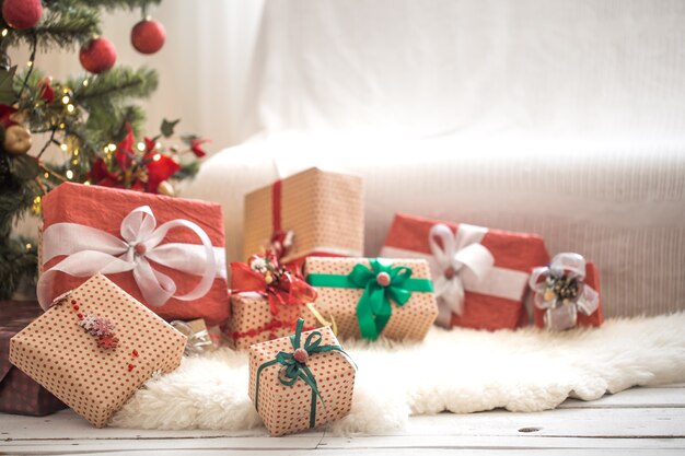 Stapel von Weihnachtsgeschenken über heller Wand auf Holztisch mit gemütlichem Teppich. Weihnachtsdekorationen