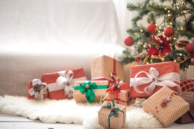 Stapel von Weihnachtsgeschenken über heller Wand auf Holztisch mit gemütlichem Teppich. Weihnachtsdekorationen