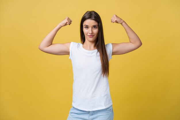 Stark und Energie. Hübsche junge Brunettefrau, die Bizeps auf ihrem Arm zeigt. Buntes Studioportrait mit gelbem Hintergrund