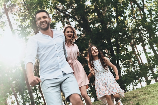 Starke familiäre bindungen. glückliche junge dreiköpfige familie, die händchen hält und beim laufen im park lächelt