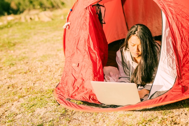 Starke Frau, die den Laptop liegt im Zelt verwendet