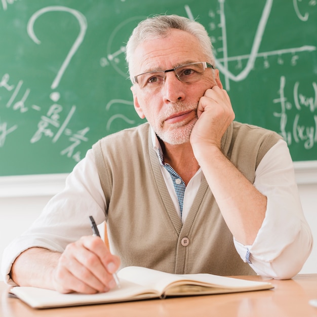 Starker gealterter Mathelehrer, der am Schreibtisch denkt