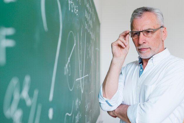 Starker gealterter Mathelehrer, der Tafel betrachtet