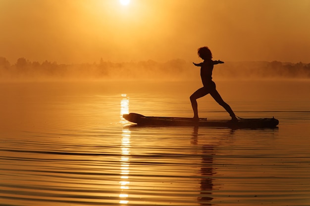 Starker junger Mann, der Yoga-Übungen auf dem Sup-Board macht