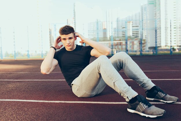 Starker Kerl mit einem guten Körpertraining am Morgen im Stadion. Er trägt Sportkleidung, Rocks Press. Er schaut in die Kamera.