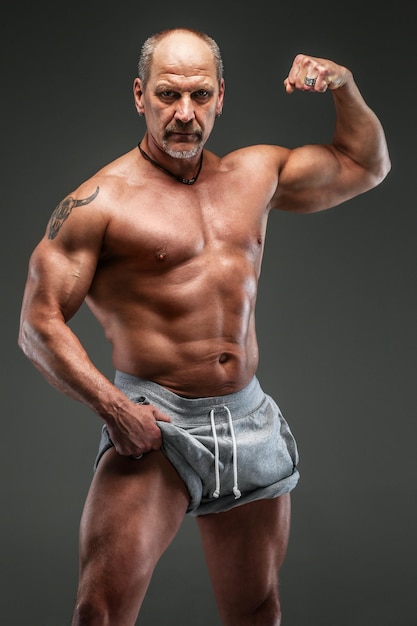 Starker muskulöser Mann mittleren Alters posiert im Studio. Isoliert auf grau.
