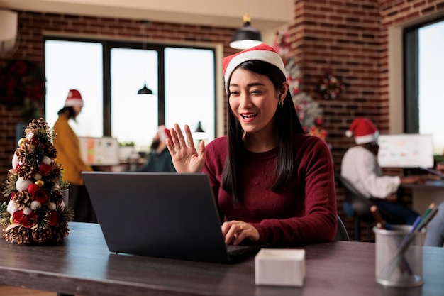 Startup-Mitarbeiter sprechen über Videoanruf im festlichen Büro, treffen sich im Online-Videokonferenz-Chat in einem mit Weihnachtsschmuck geschmückten Raum. Frau, die bei einem Remote-Telefonkonferenzanruf chattet.