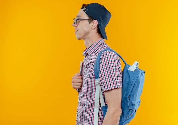 Kostenloses Foto stehen in der profilansicht junger studentjunge, der rückentasche und brille und kappe auf weiß trägt