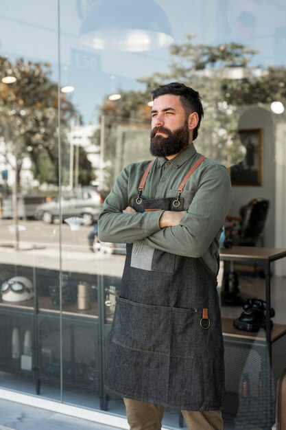 Stehender äußerer naher Friseursalon des bärtigen ernsten Friseurs