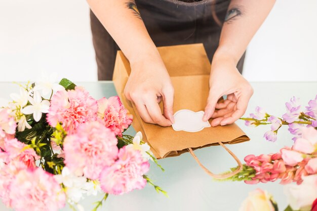 Stehender Aufkleber der Floristenhand auf Papiertüte mit Blumen auf Schreibtisch