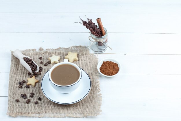 Sternplätzchen, Kaffeebohnen, Tasse Kaffee auf einem Stück Sack mit Schüssel Instantkaffee, Glaskräuter-Hochwinkelansicht auf einem weißen Holzbretthintergrund