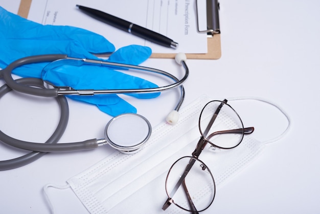 Kostenloses Foto stethoskop im arztschreibtisch, medizinisches konzept. coronavirus (covid-19. stethoskop, brille und gesichtsmaske auf weißem schreibtisch. schutz vor viren, coronaviren, grippe, erkältungen, krankheiten. flache draufsicht