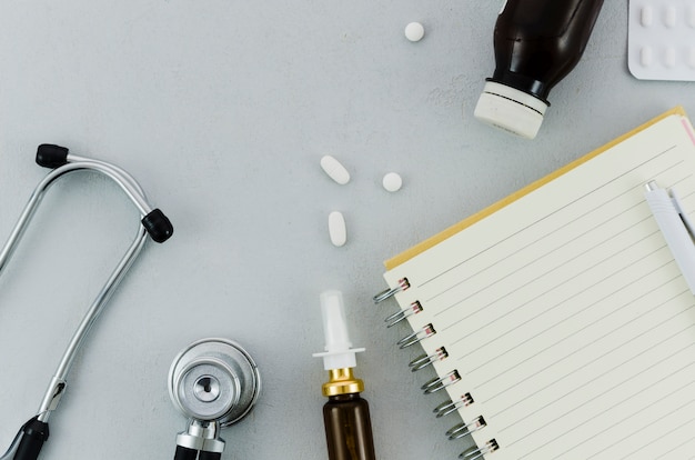 Stethoskop; Pillen; Flasche; Nasenspray; Tagebuch und Stift auf grauem Hintergrund