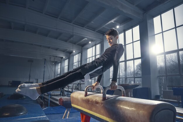 Steuerung. Kleines männliches Turnertraining im Fitnessstudio, flexibel und aktiv. Kaukasischer kleiner Junge, Athlet in Sportbekleidung, der in Übungen für Kraft, Gleichgewicht praktiziert. Bewegung, Aktion, Bewegung, dynamisches Konzept.