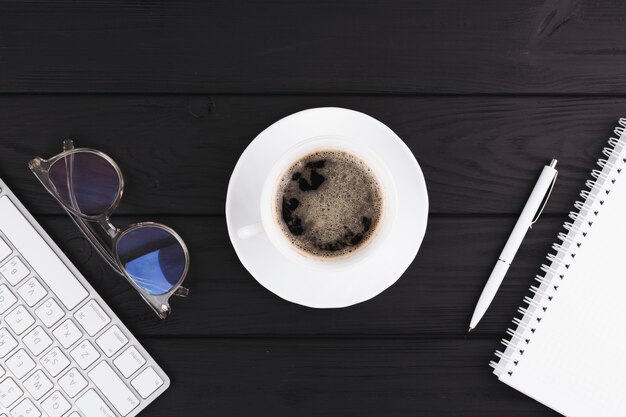 Stift in der Nähe von Notebook, Tasse auf Untertasse, Brillen und Tastatur