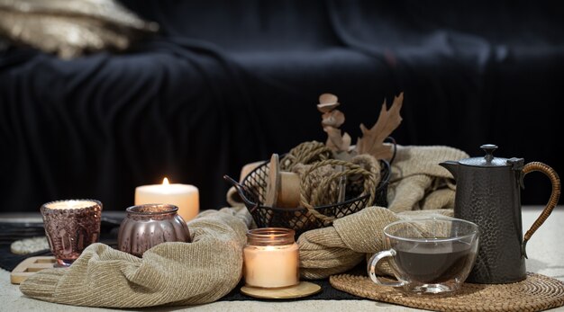 Stillleben auf dem Tisch mit Kerzen, Pulloverbuch und Herbstlaub. Gemütliches Wohnzimmer, Inneneinrichtung.