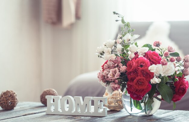 Stillleben mit einem Inschriftenhaus und einer Vase mit Blumen verschiedener Rosen. Das Konzept von Wohnkomfort und Dekor.