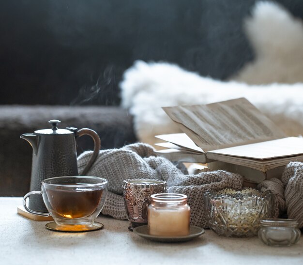 Stillleben mit einer Tasse Tee, einer Teekanne, einem Buch und wunderschönen Vintage-Kerzenleuchtern mit Kerzen. Wohnkultur-Konzept.