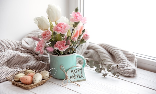 Stillleben mit frischen frühlingsblumen in einer vase, eiern, einer frohe osterkarte und einem gestrickten element.