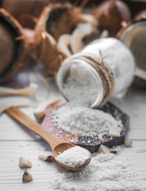 Stillleben mit Kokosnuss und Kokosflocken in Holzlöffeln und Glas auf Holzhintergrund