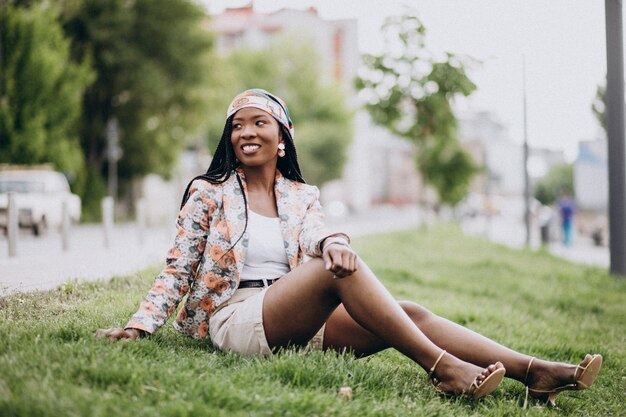 Stilvolle Afroamerikanerfrau im Park, der auf Gras sitzt