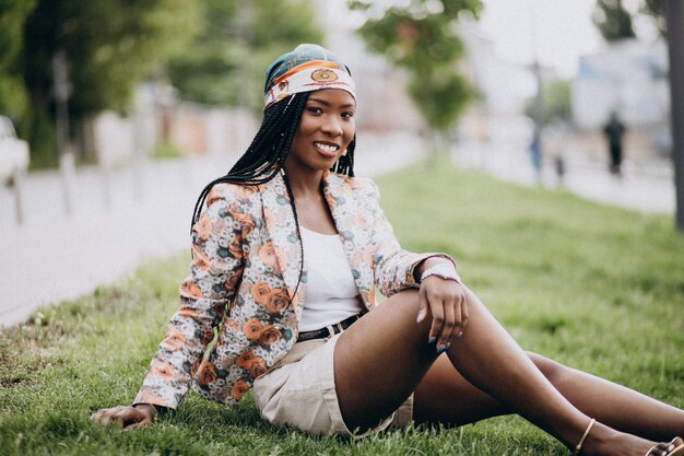 Stilvolle Afroamerikanerfrau im Park, der auf Gras sitzt