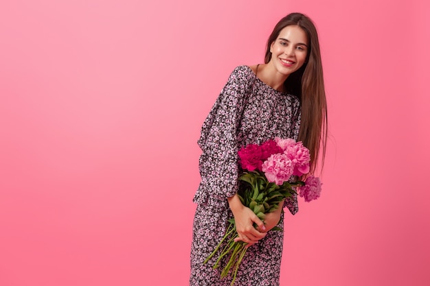 Stilvolle Frau auf Rosa im trendigen Sommerkleid, das mit Pfingstrosenblumenstrauß aufwirft