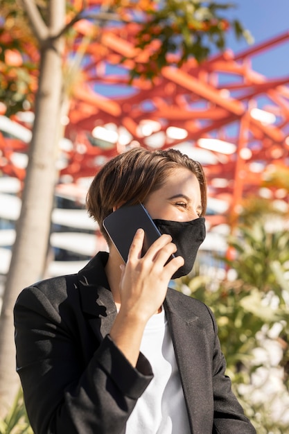 Stilvolle Frau, die am Telefon spricht, während sie eine medizinische Maske trägt