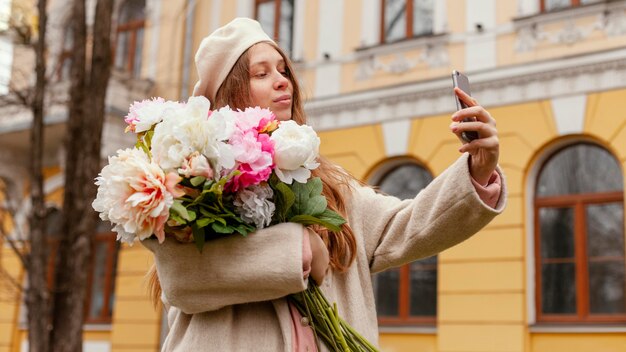 Stilvolle Frau, die Blumenstrauß draußen im Frühling hält und selfie nimmt