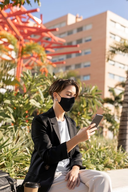 Kostenloses Foto stilvolle frau, die ihr telefon beim tragen einer medizinischen maske hält