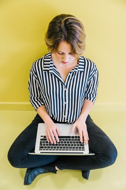 Stilvolle Frau, die Laptop auf Gelb verwendet