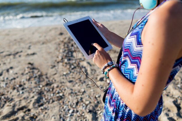 Stilvolle Frau, die Tablette verwendet und auf tropischem Strand geht