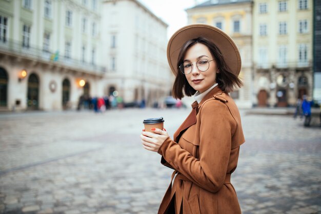 Stilvolle Frau im breiten Hut, der Kaffee auf Herbststadt trinkt