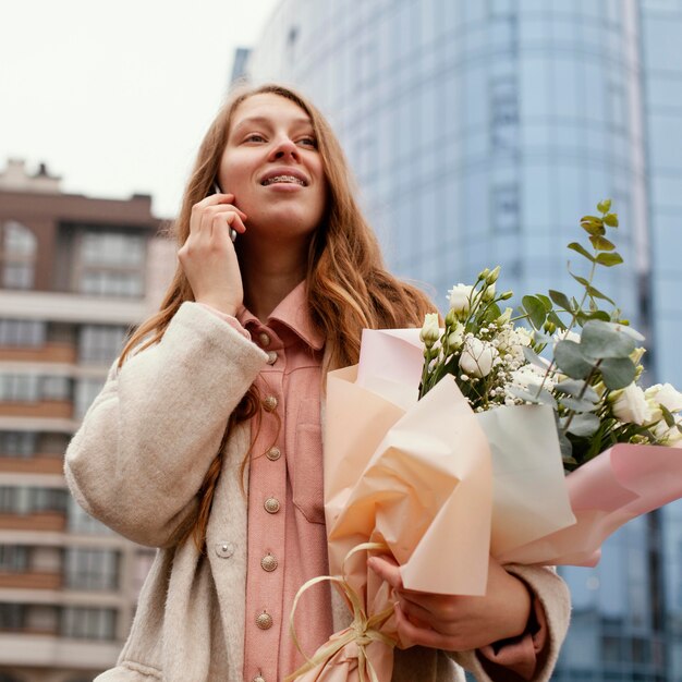 Stilvolle Frau im Freien, die am Telefon unterhält und Blumenstrauß hält