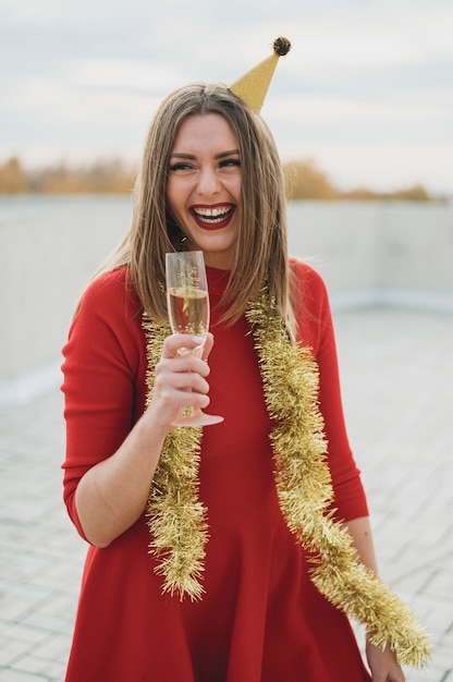 Stilvolle Frau im roten Kleid, das ein Glas Champagner und ein Lächeln hält