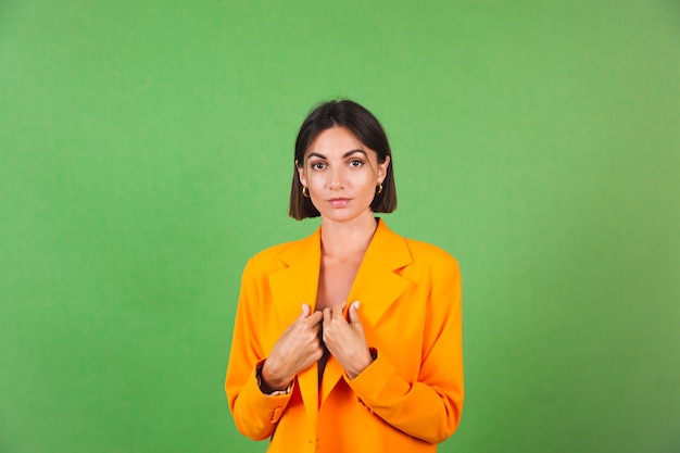 Stilvolle Frau in seidenbeigem Kleid und orangefarbenem übergroßem Blazer auf grünem, positivem Emotionenlächeln