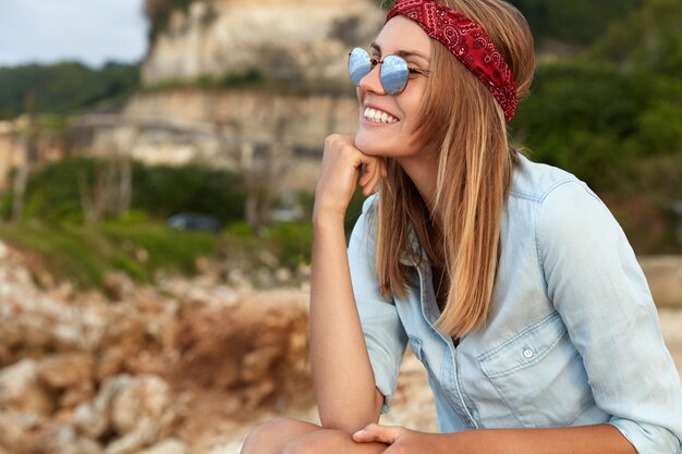 Stilvolle Frau mit Sonnenbrille, die am Strand sitzt