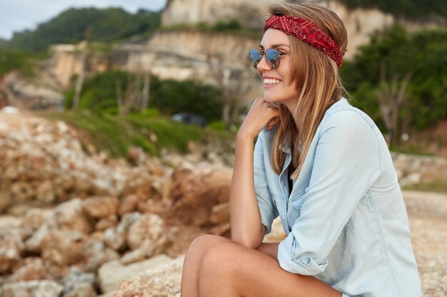 Stilvolle Frau mit Sonnenbrille, die am Strand sitzt