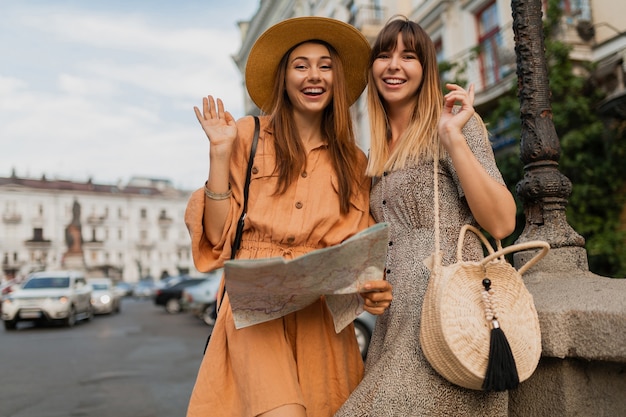 Stilvolle junge Frauen, die zusammen in Europa reisen, gekleidet in trendigen Frühlingskleidern und Accessoires mit Karte