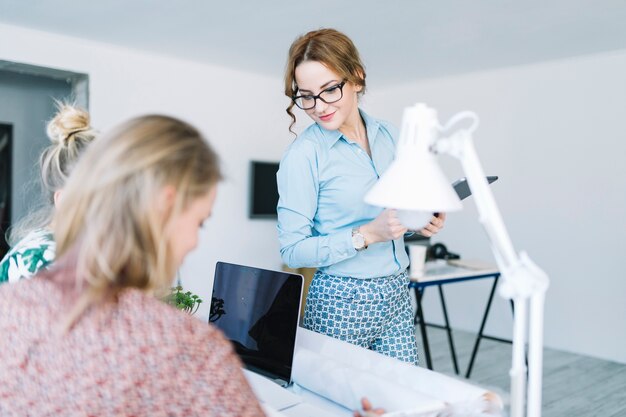 Stilvolle junge Geschäftsfrau, die weibliches Arbeiten zwei am Arbeitsplatz betrachtet