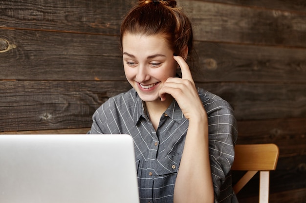 Kostenloses Foto stilvolle junge rothaarige frau im grauen hemd, das im café vor offenem laptop sitzt