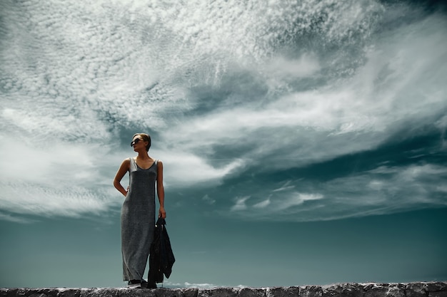 stilvolle Mädchenfrau in lässiger Hipster-Kleidung, die hinter Himmel mit Wolken aufwirft